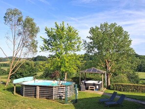 Une piscine avec un jacuzzi, des chaises longues et un kiosque, le tout situé dans un jardin verdoyant avec des arbres.