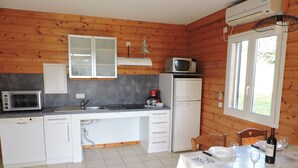 Una cocina compacta con armarios blancos, microondas, refrigerador y un comedor con una mesa para dos.