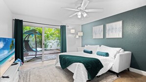 Une chambre avec un lit, un ventilateur de plafond et une vue sur un patio équipé d’une chaise et d’un parasol.