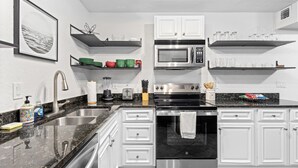 Une cuisine moderne avec des meubles blancs, un évier en acier inoxydable, un four à micro-ondes et une cuisinière.