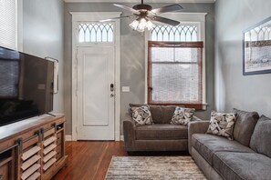 A living room with a grey sofa, a television on a wooden stand, and a ceiling fan. - Valence St Charmer, Walk to Freret & Tulane (New Orleans)