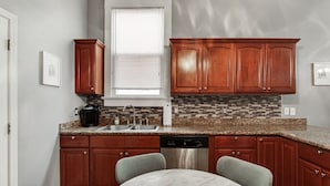 Una cocina con armarios de madera, encimera de granito, lavavajillas y mesa de mármol.