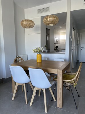 Un coin repas avec une table en bois, des chaises blanches et un vase jaune orné de fleurs.