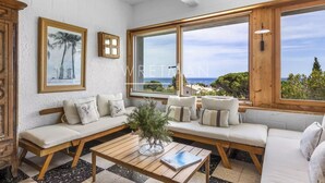 Ein geräumiges Wohnzimmer mit großem Fenster und Meerblick, einem Holztisch und einer Sofagarnitur mit gemusterten Kissen.