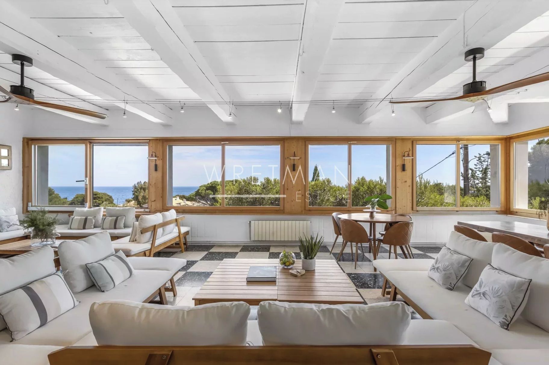 A spacious living area with large windows, a wooden ceiling, and a view of the sea.
