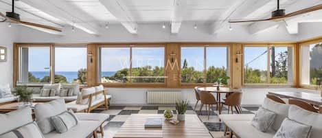 A spacious living area with large windows, a wooden ceiling, and a view of the sea.