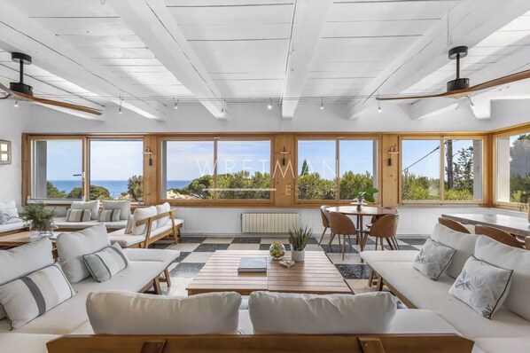 A spacious living area with large windows, a wooden ceiling, and a view of the sea.