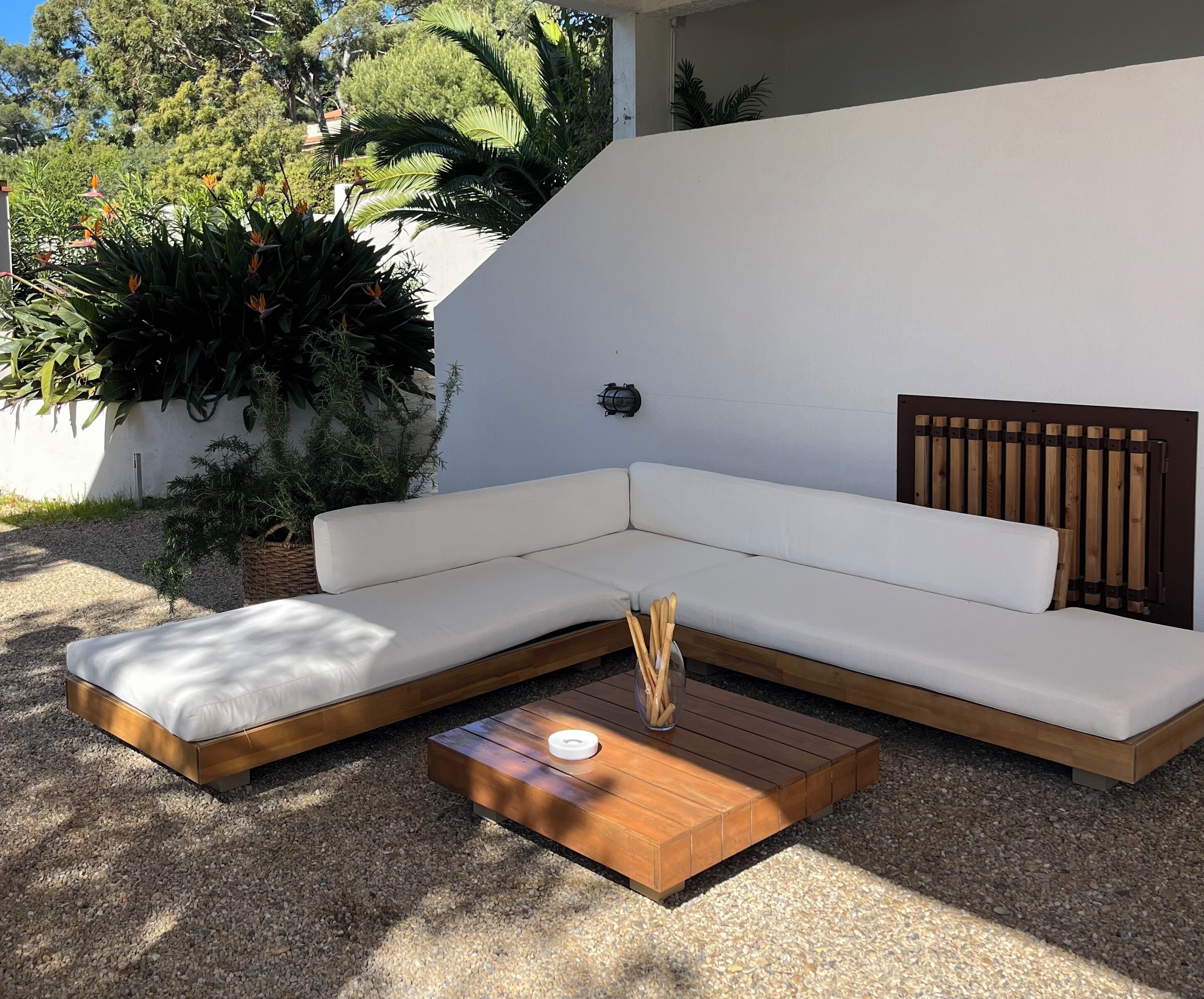Un espace de détente extérieur moderne, comprenant un canapé d’angle, une petite table en bois et un banc rembourré.