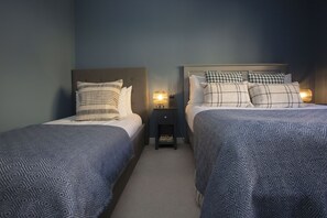A hotel room with two beds, each with a headboard, a bedside table, and a lamp.