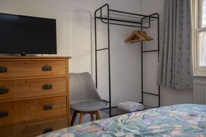 A bedroom with a bed, a dresser, a chair, a TV, and a metal rack with a towel.