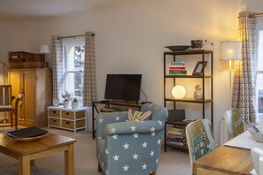 A cozy living room with a star-patterned armchair, a wooden table, a bookshelf, and a television.
