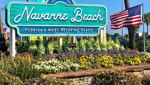 A sign welcoming visitors to Navarre Beach, Florida, with a colorful garden in front. - Emerald Coast Stay! (Navarre)