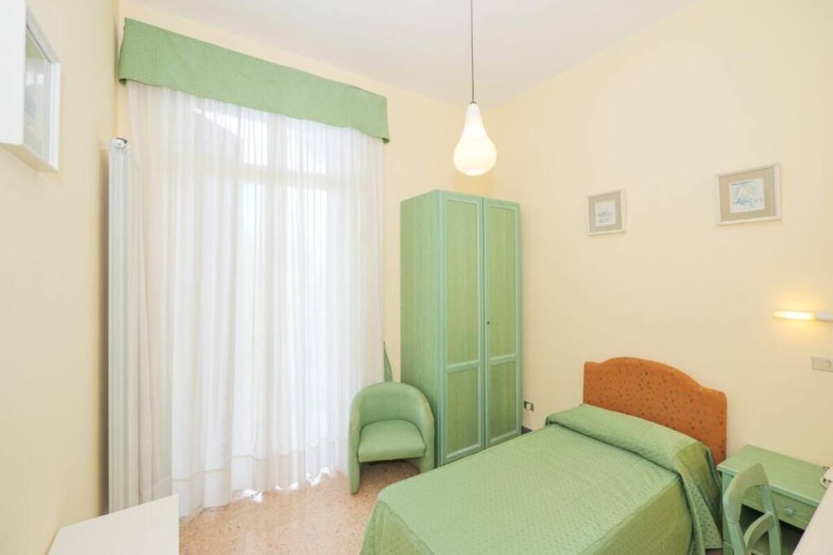 Une chambre à coucher comprenant un lit, une chaise, un bureau, une armoire et un luminaire suspendu.