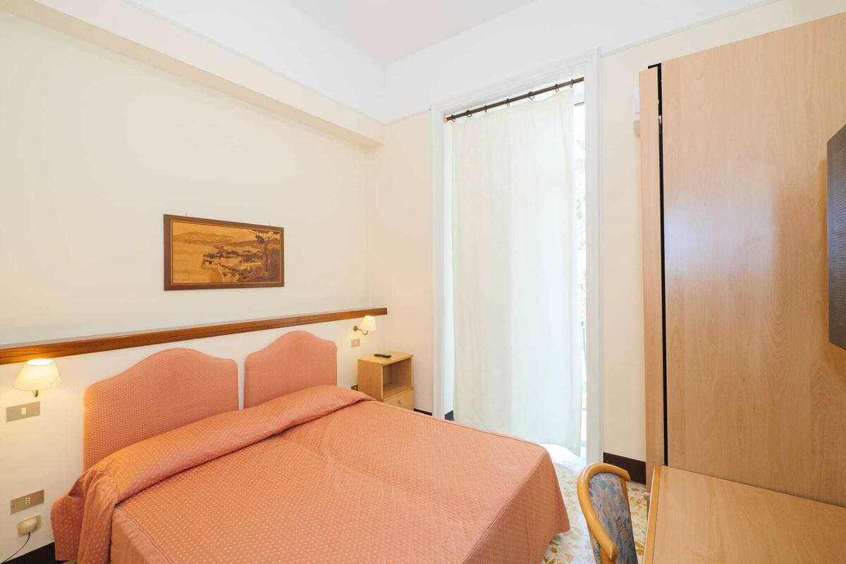 Une chambre d’hôtel avec un lit, une table de chevet, une lampe, un tableau au mur et une armoire.