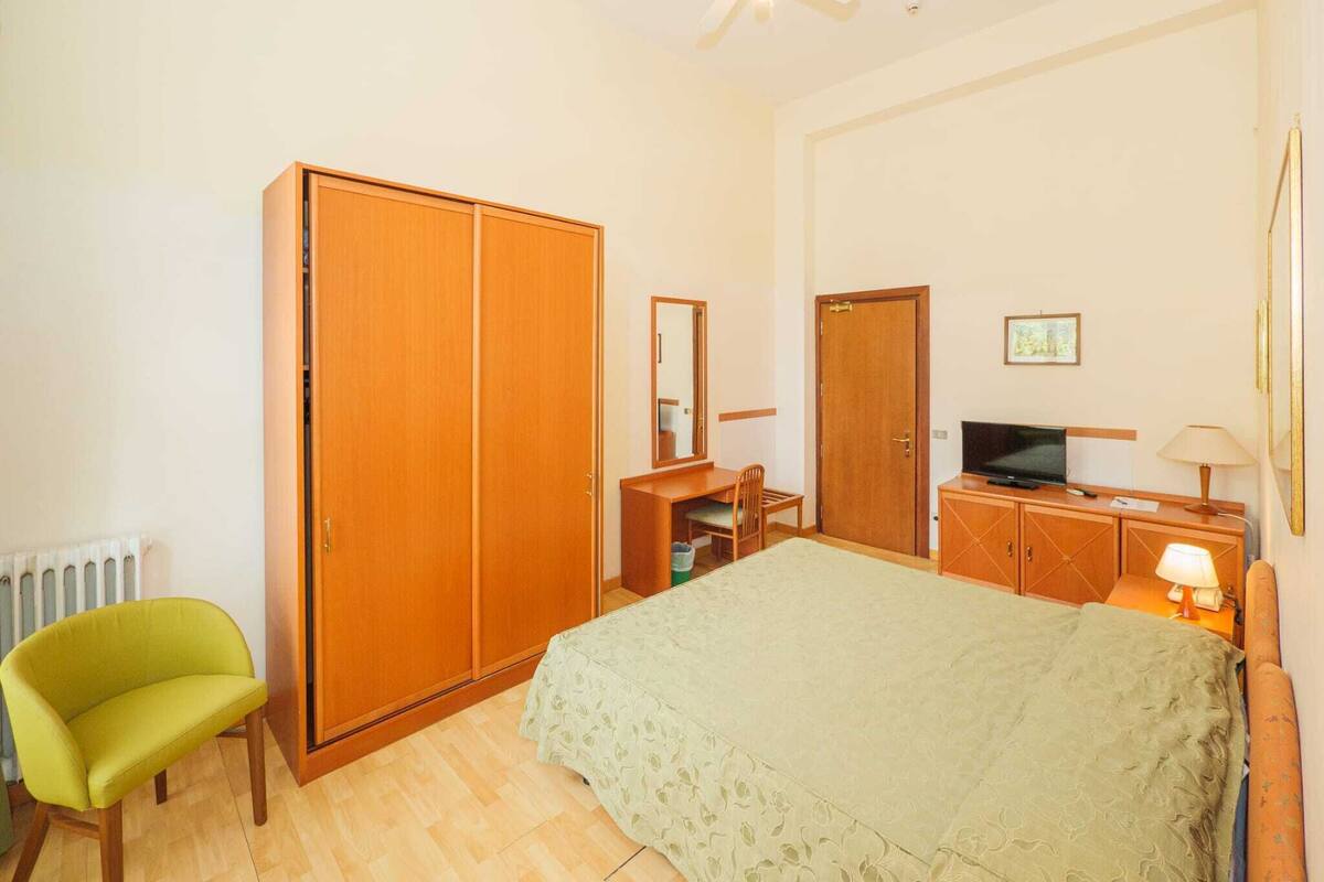Une chambre à coucher comprenant un lit, une armoire, un bureau avec une chaise, un téléviseur et un radiateur.