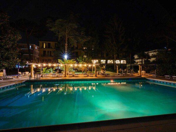 Un espace piscine nocturne avec des chaises longues et un coin salon abrité.