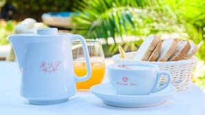 Een gedekte tafel met een witte theepot, een glas sinaasappelsap, een kop koffie en een mand met brood.