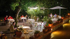 Een buitenontbijtplaats met tafels en stoelen, omringd door groen en een waterpartij.