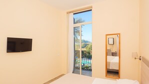 Een hotelkamer met een bed, een aan de muur bevestigde televisie, een spiegel in de badkamer en een glazen schuifdeur die uitkomt op een zwembad.