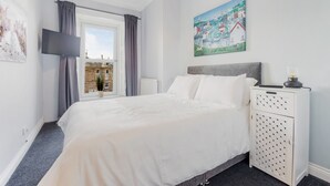A bedroom with a large bed, a nightstand with drawers, a flat-screen TV, and a window with curtains.