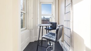 A narrow hallway with a small table and two chairs, a window, and a radiator.