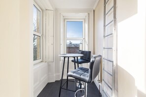 A narrow hallway with a small table and two chairs, a window, and a radiator.