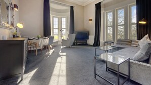 A modern living room with a sofa, a glass coffee table, a TV, and a dining area with chairs and a table.
