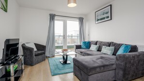 A modern living room with a grey sofa, a TV, and a coffee table. - Impeccable 2-bed Apartment in Romford (Romford)