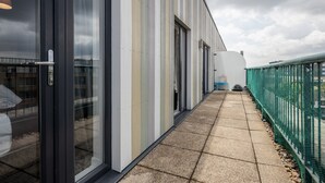 A corridor with a glass door, a tiled walkway, and a green fence. - Impeccable 2-bed Apartment in Romford (Romford)