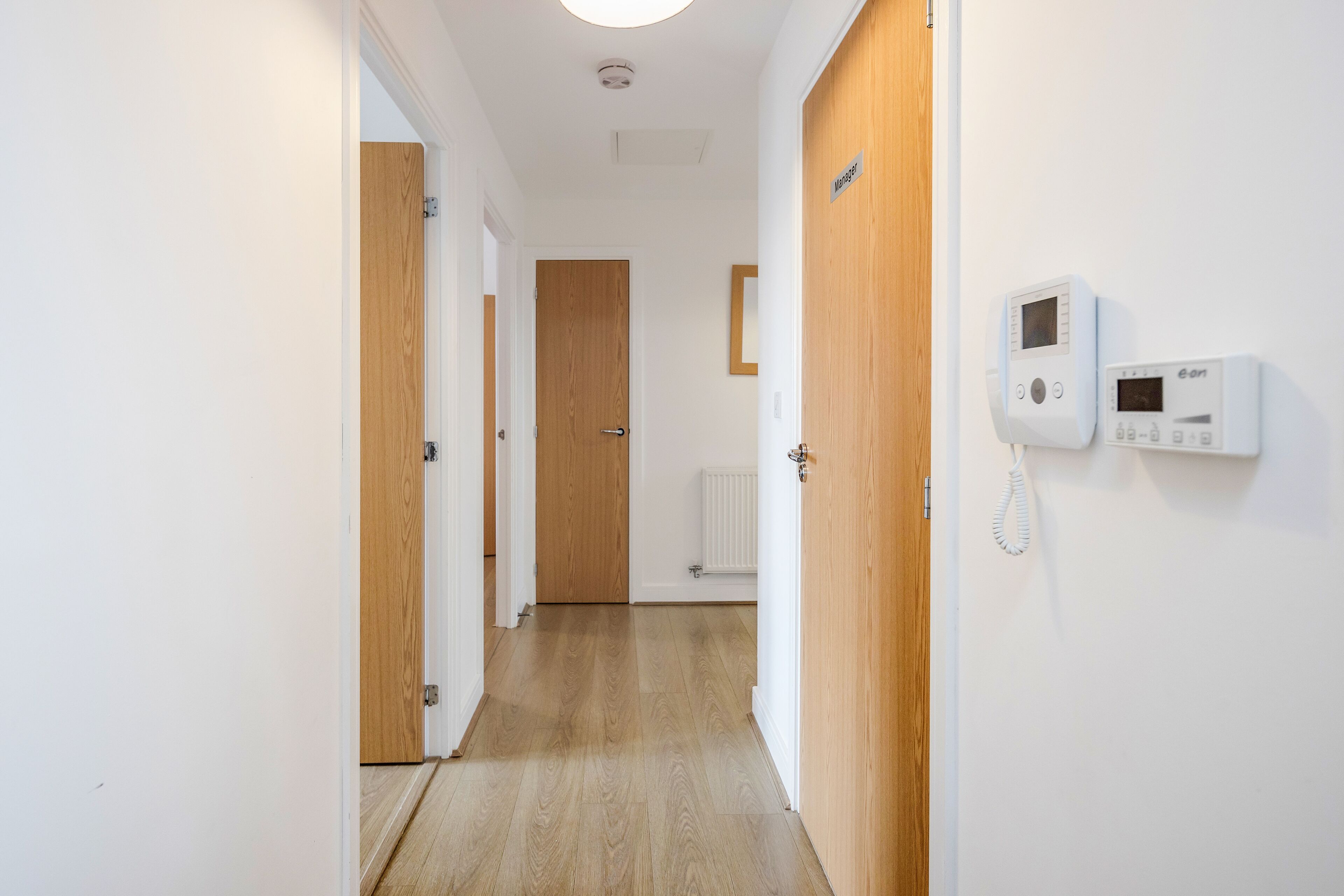 Ein Korridor mit Holztüren, einem weißen, an der Wand montierten Gegensprechanlage und einem Heizkörper.