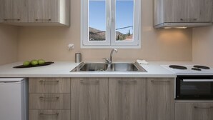A kitchen with a double sink, wooden cabinets, a stove, and a window with a view of a hilly landscape. - Close to the beach, spacious one-bedroom apartment with sea views. (Corfu)