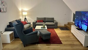 A modern living room with a grey sofa, a grey armchair, a white coffee table, and a flat-screen TV on a white stand.
