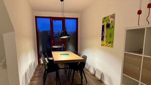 A dining area with a wooden table and black chairs, a pendant light, and a view through a window with red framing.