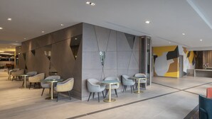 A modern interior with a seating area featuring round tables and chairs, a geometric wall design, and a visible ceiling with recessed lighting. - Maldron Hotel Merrion Road (Dublin)