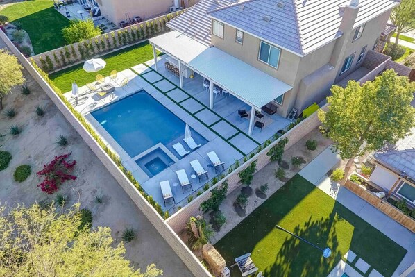 A modern house with a large swimming pool, covered patio, and a well-maintained lawn.