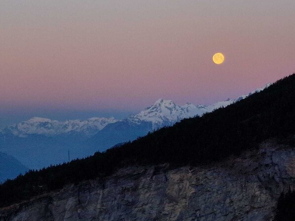 A mountain landscape with a visible moon in the sky.