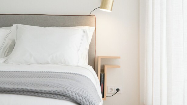 A neatly made bed with white linens, a grey blanket, and a wooden bedside table with a lamp. - Souto Apartments (Porto)