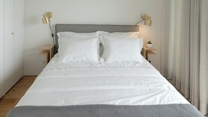 A neatly made bed with white linens, two bedside lamps, and a small cactus on a bedside table. - Souto Apartments (Porto)