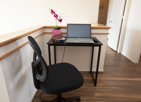 Un espace de travail avec un ordinateur portable sur un bureau, une chaise, une orchidée en pot et un carnet.