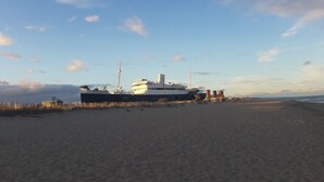 Ein großes Schiff liegt an einem sandigen Strand unter blauem Himmel.