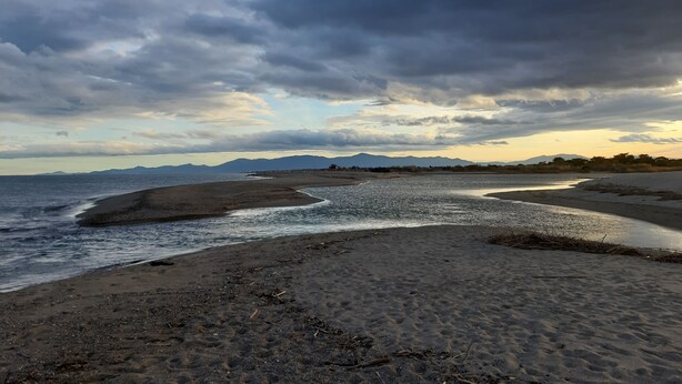 Ein Strand mit weitem Sandbereich, ruhigem Meer und fernen Bergen unter einem bewölkten Himmel.