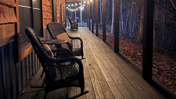 Une terrasse en bois, agrémentée de chaises et d’une table en osier, qui offre une vue sur une zone boisée.