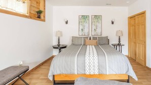 Une chambre avec un grand lit, deux tables de chevet, un banc, un banc en bois, une fenêtre avec des rideaux et une porte en bois.
