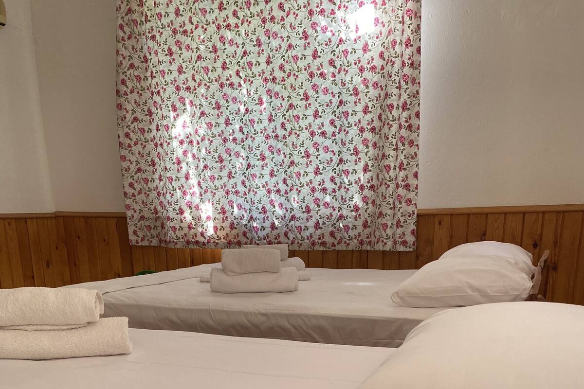 A hotel room with two beds, wooden headboards, and a floral curtain.