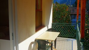 A balcony with a table and chairs, a window, and a view of trees and mountains.