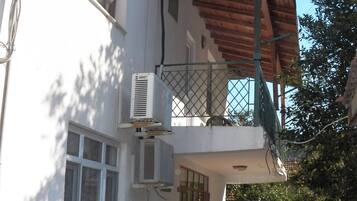 Un edificio de dos pisos con balcón, aire acondicionado y plantas en macetas.