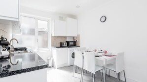 A modern kitchen with white cabinetry, a built-in microwave, and a coffee machine. - Charming 3-bed Apartment in Romford (Romford)