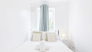 A minimalist bedroom with a large bed, white bedding, and a window with curtains. - Charming 3-bed Apartment in Romford (Romford)