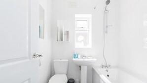 A small, white bathroom with a toilet, sink, and bathtub. - Charming 3-bed Apartment in Romford (Romford)