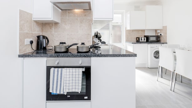 A modern kitchen with white cabinets, a built-in oven, a coffee maker, and a microwave. - Charming 3-bed Apartment in Romford (Romford)